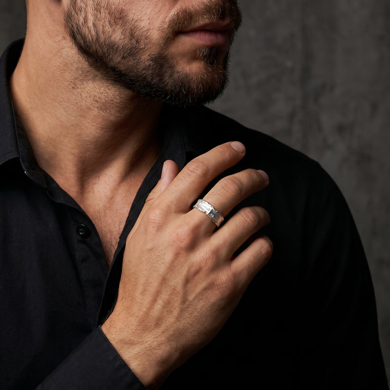 Man wearing the textured silver starburst open-band ring on a finger near his chest, against a black shirt.