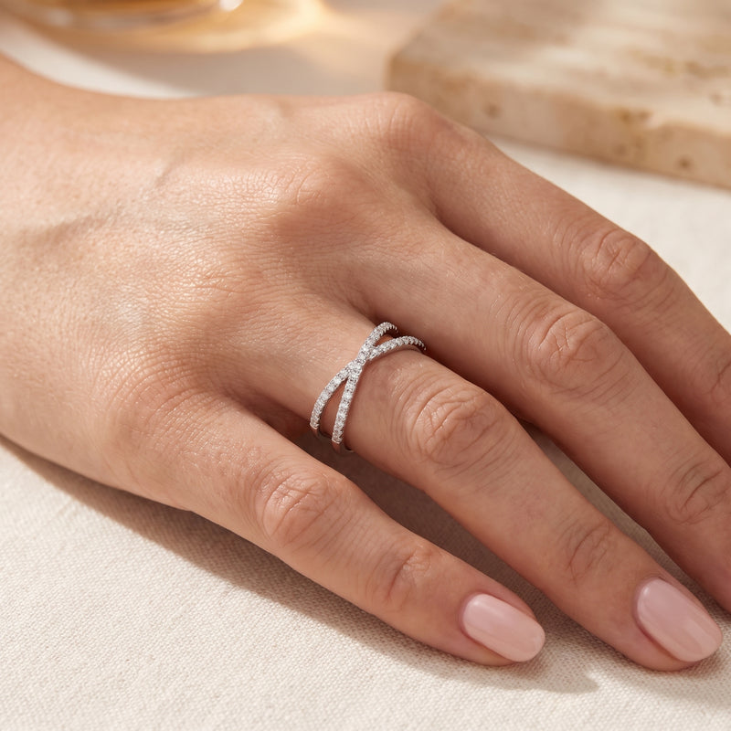 Silver crossover ring with small clear stones worn on a hand with nude manicured nails.