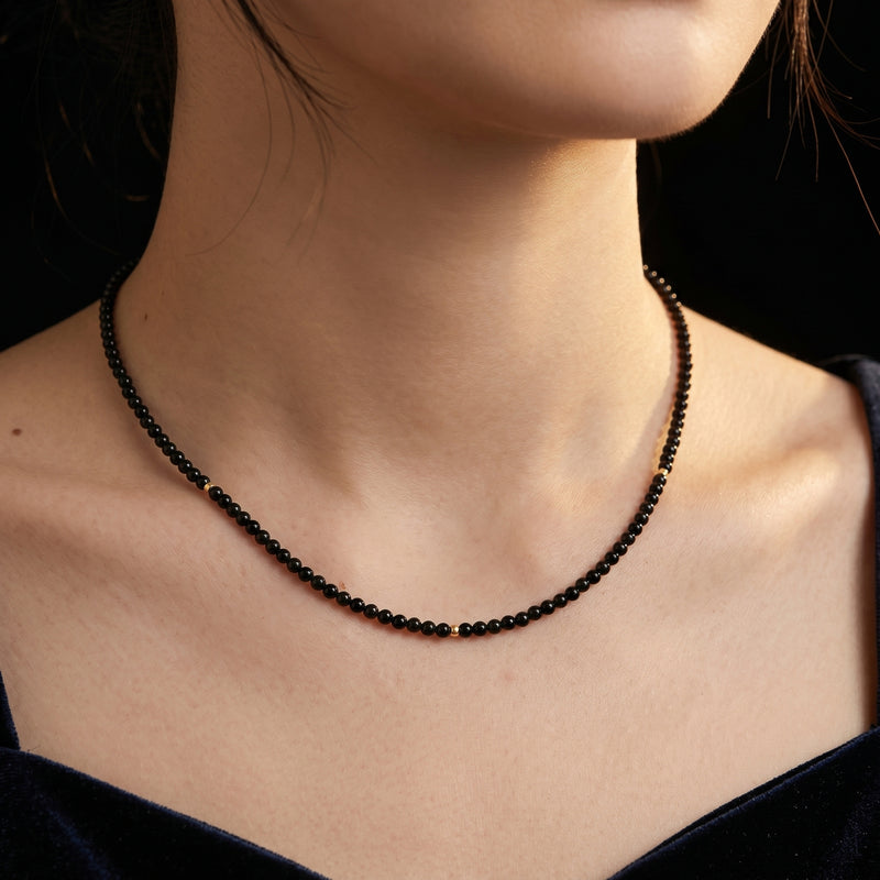 Close-up of a woman wearing the 15-inch solid gold necklace with 3mm polished natural black onyx beads.