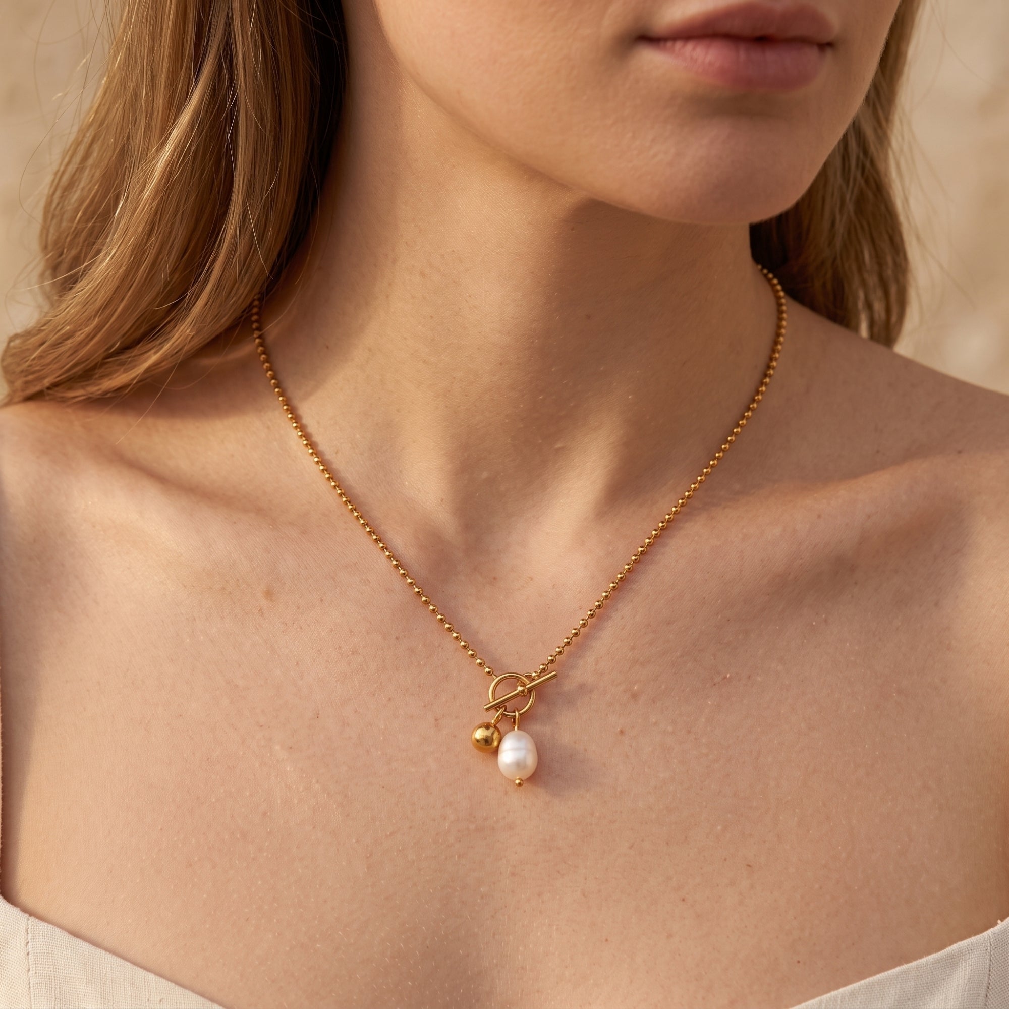 Gold stainless steel necklace with baroque pearl and toggle clasp worn by a model.