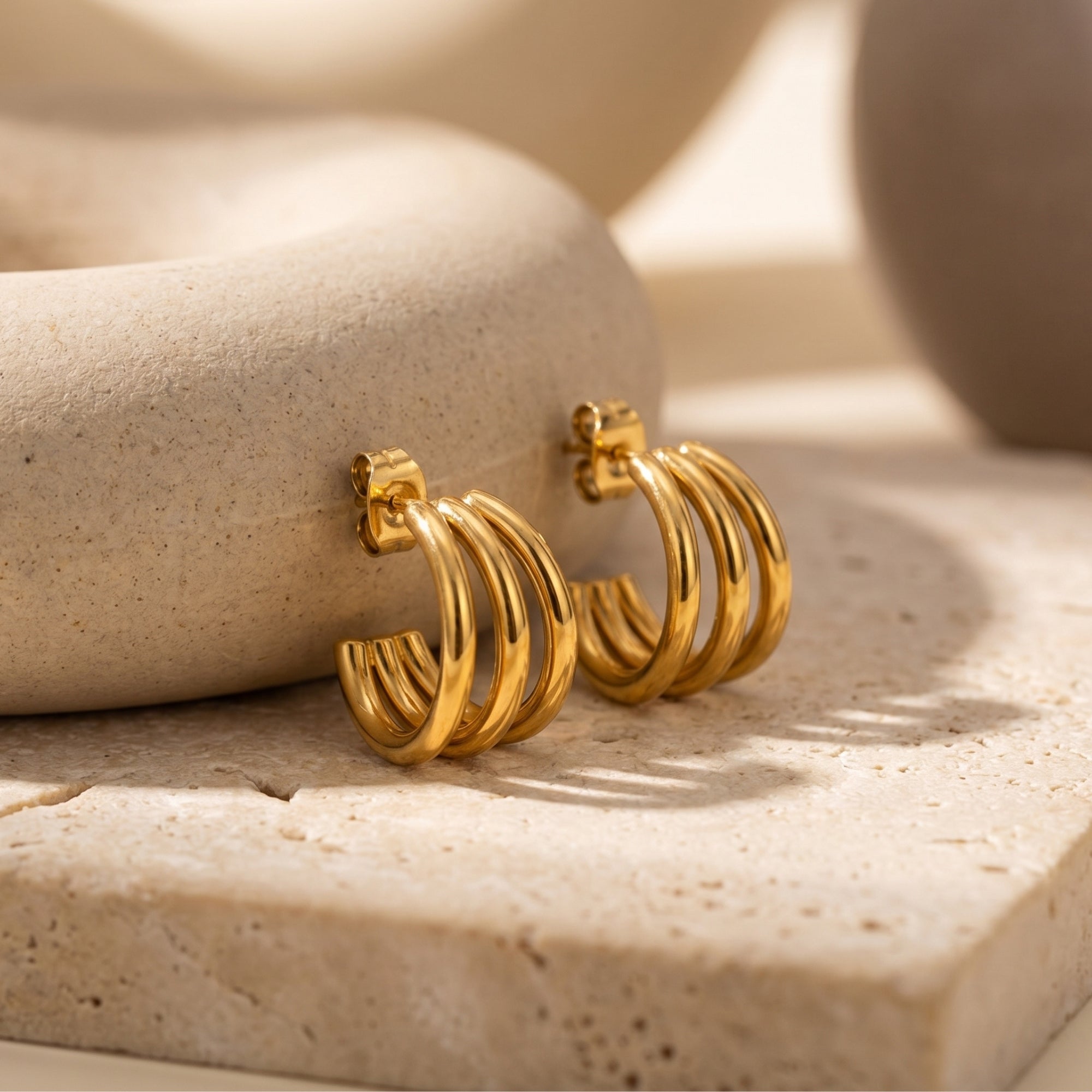 Close-up of gold triple-band hoop earrings showing the stacked architectural design.