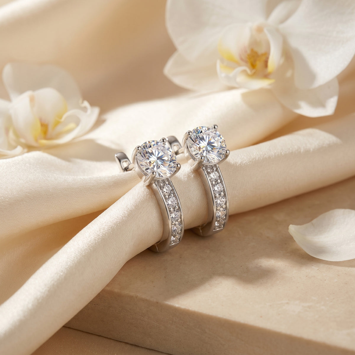 Silver moissanite hoop earrings with round cut stones on white silk with flowers.