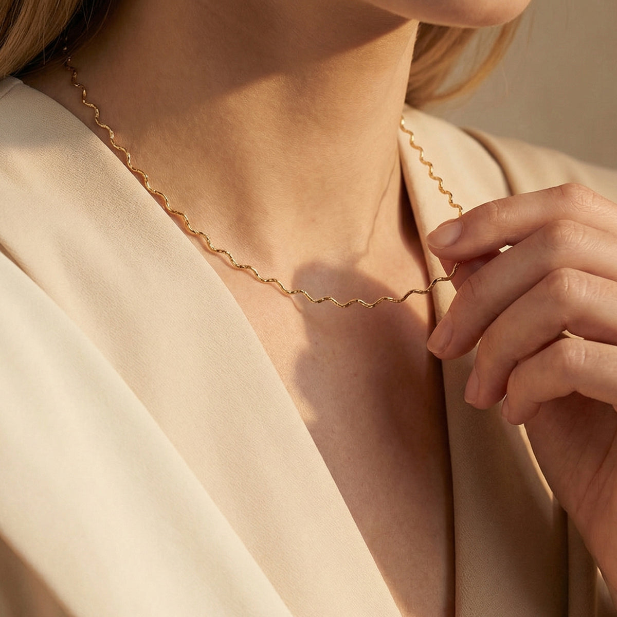 Close-up of a model wearing the gold-toned wavy chain necklace and touching it near the collarbone.