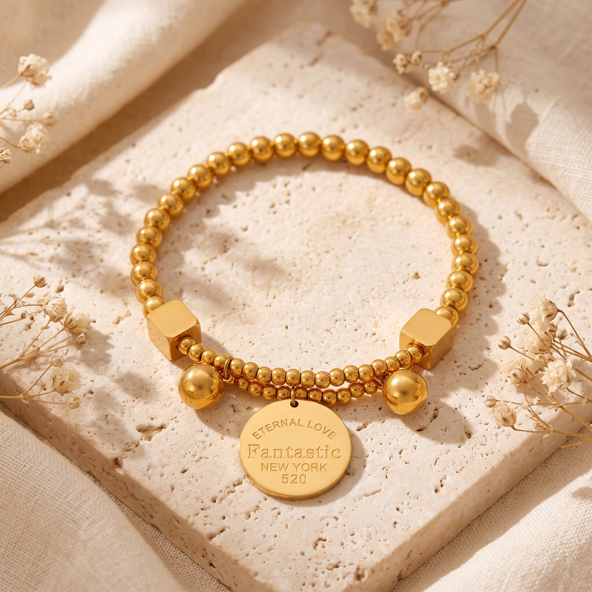 Top-down view of the gold-tone beaded bracelet with a stamped disc charm lying on a stone surface.