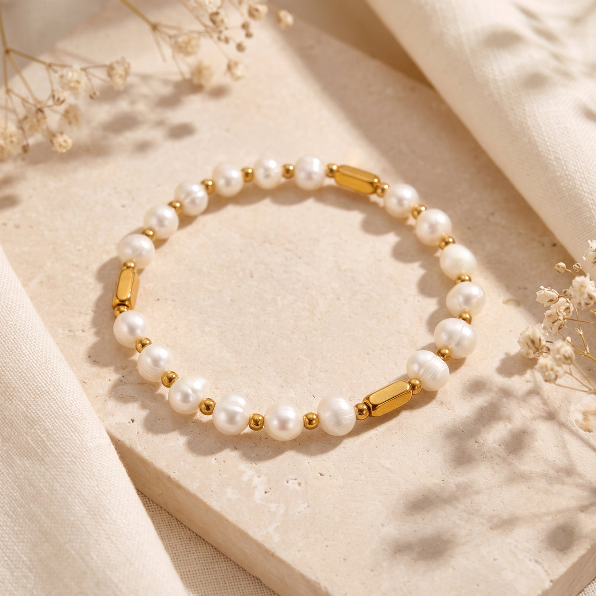 Angled view of the pearl and gold-color station bracelet arranged on a stone slab beside light fabric.