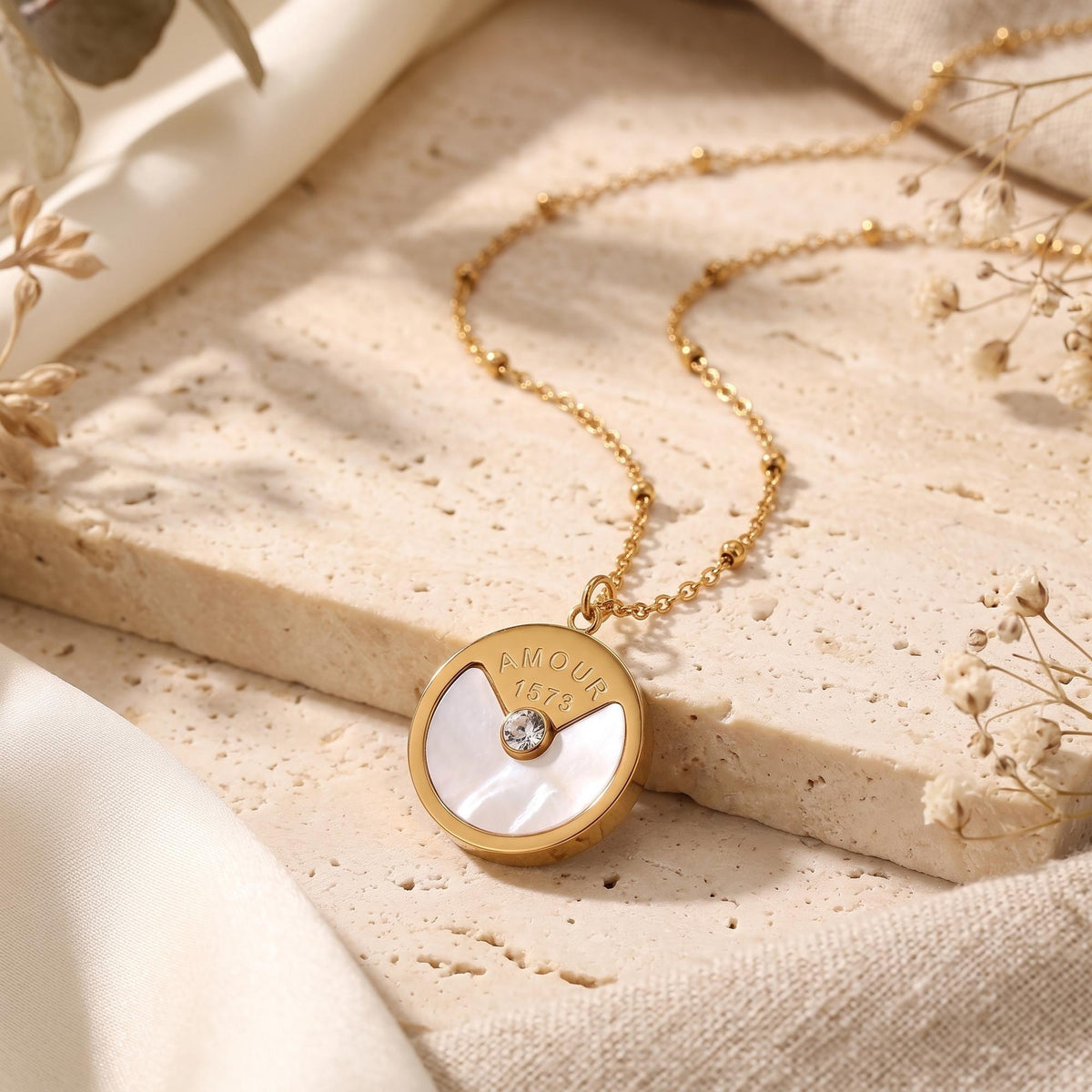 Macro view of gold 'Amour' engraved pendant with mother-of-pearl inlay and round cubic zirconia.