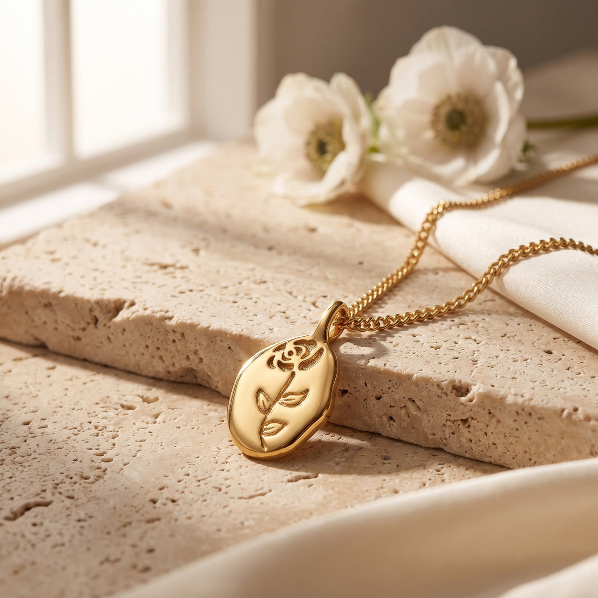Close-up of the etched rose motif on the organic oval 18K gold finish pendant.