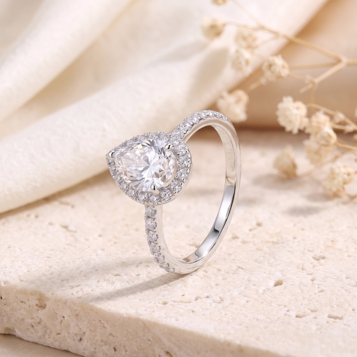 Angled view of the ring showing the pear-shaped halo setting, partial pavé band, and plain inner shank.