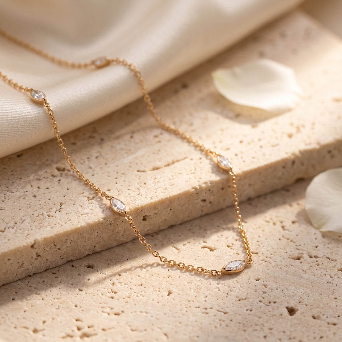 Gold-tone station necklace with clear marquise stones draped across a textured beige stone surface.