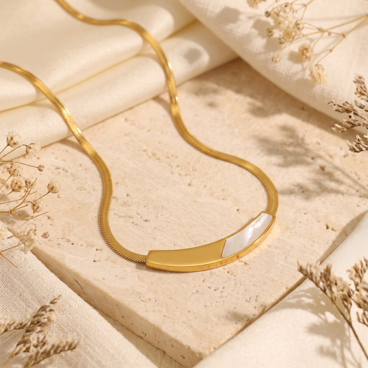 Close-up of a gold stainless steel snake chain necklace featuring a curved mother of pearl inlay.