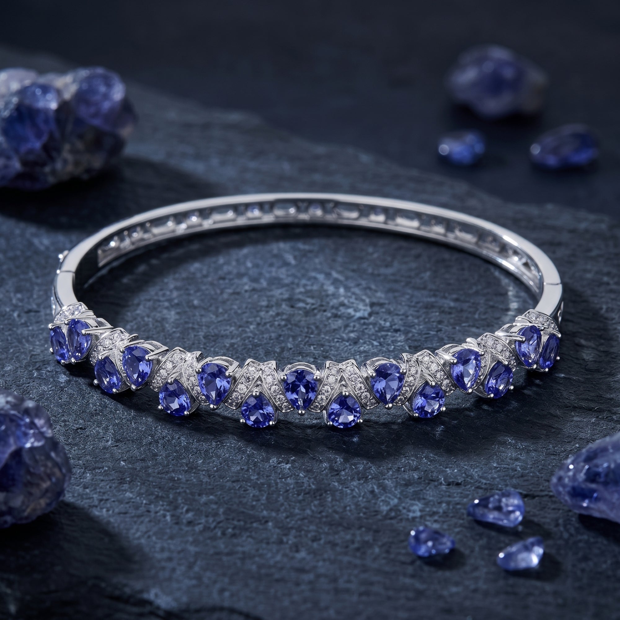 Pear-cut tanzanite and white gold bracelet resting on a dark stone surface with raw tanzanite crystals.