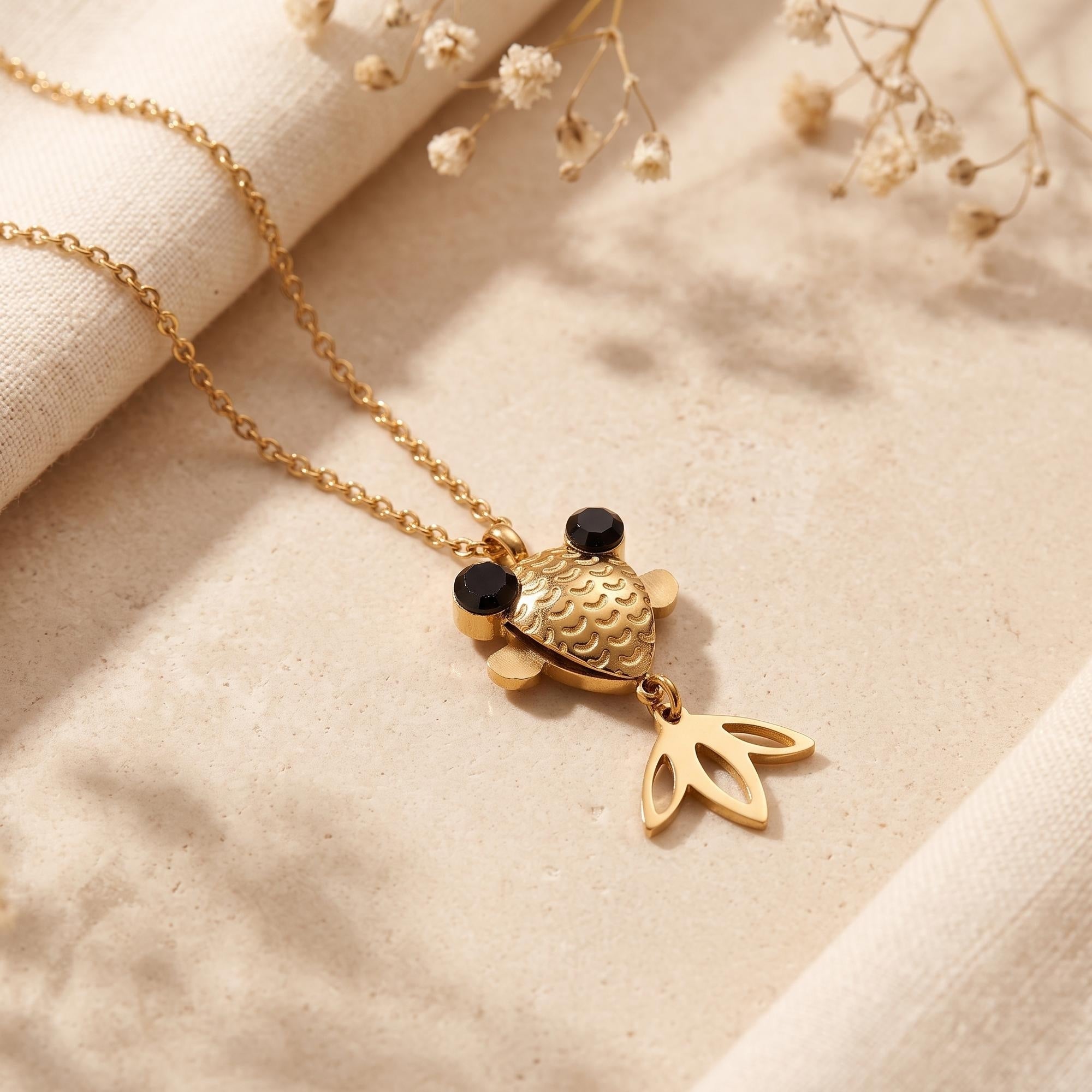 Macro view of a gold finish stainless steel goldfish pendant showing scale details and black eyes.