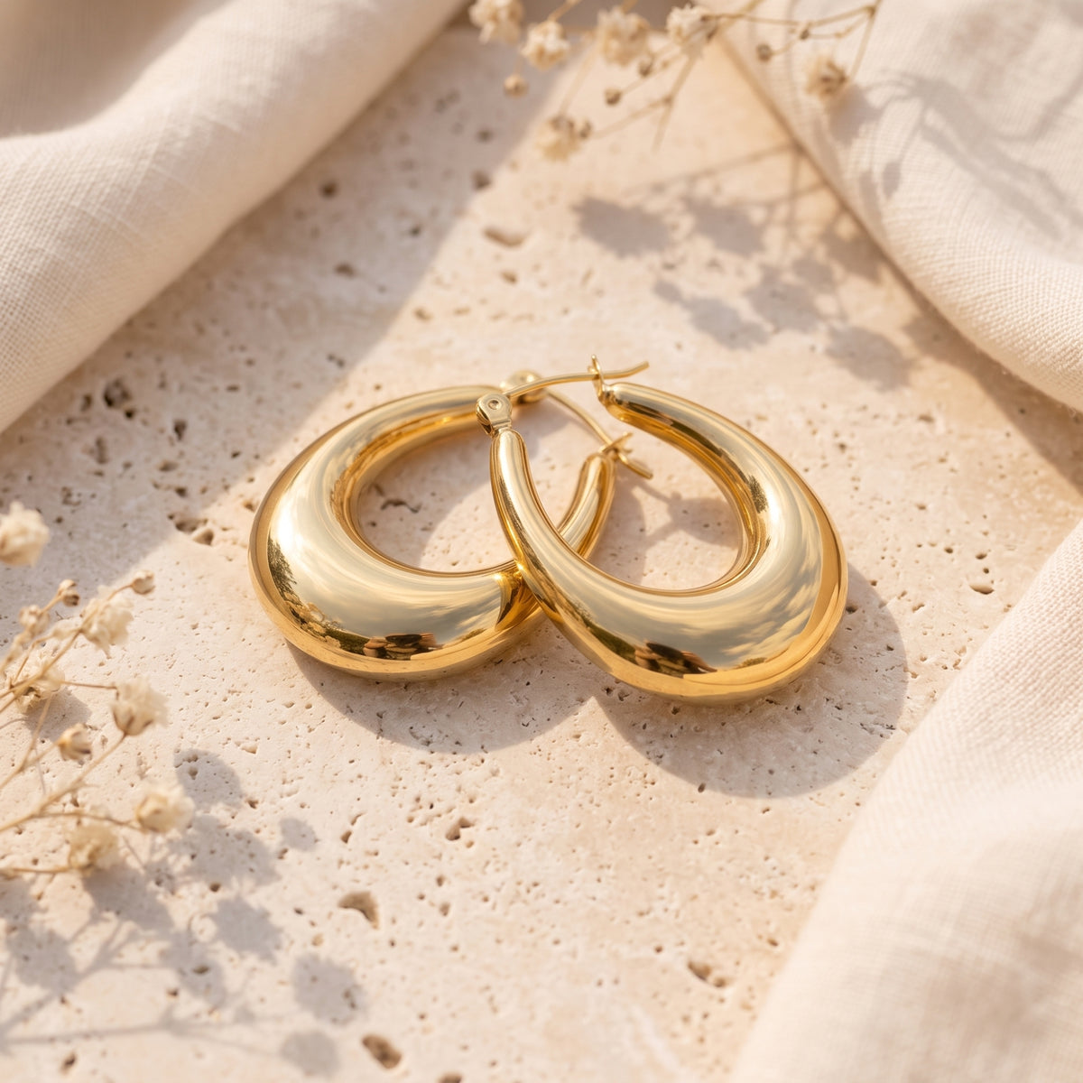 Pair of polished gold-tone teardrop earrings lying flat on a textured stone surface.