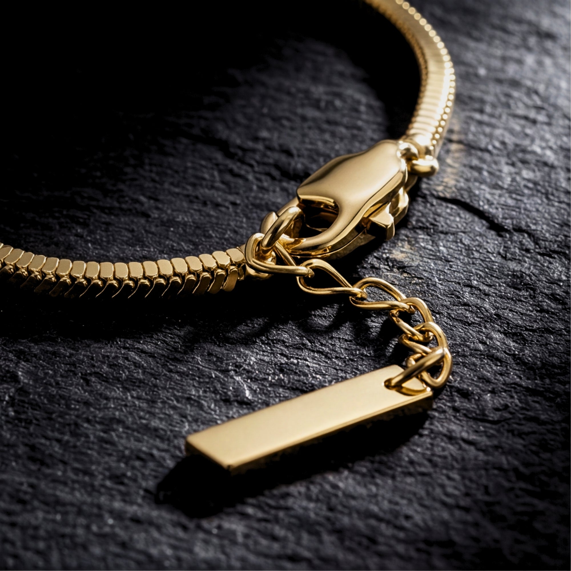 Macro view of the lobster clasp and logo tag on a gold-tone stainless steel square link bracelet.