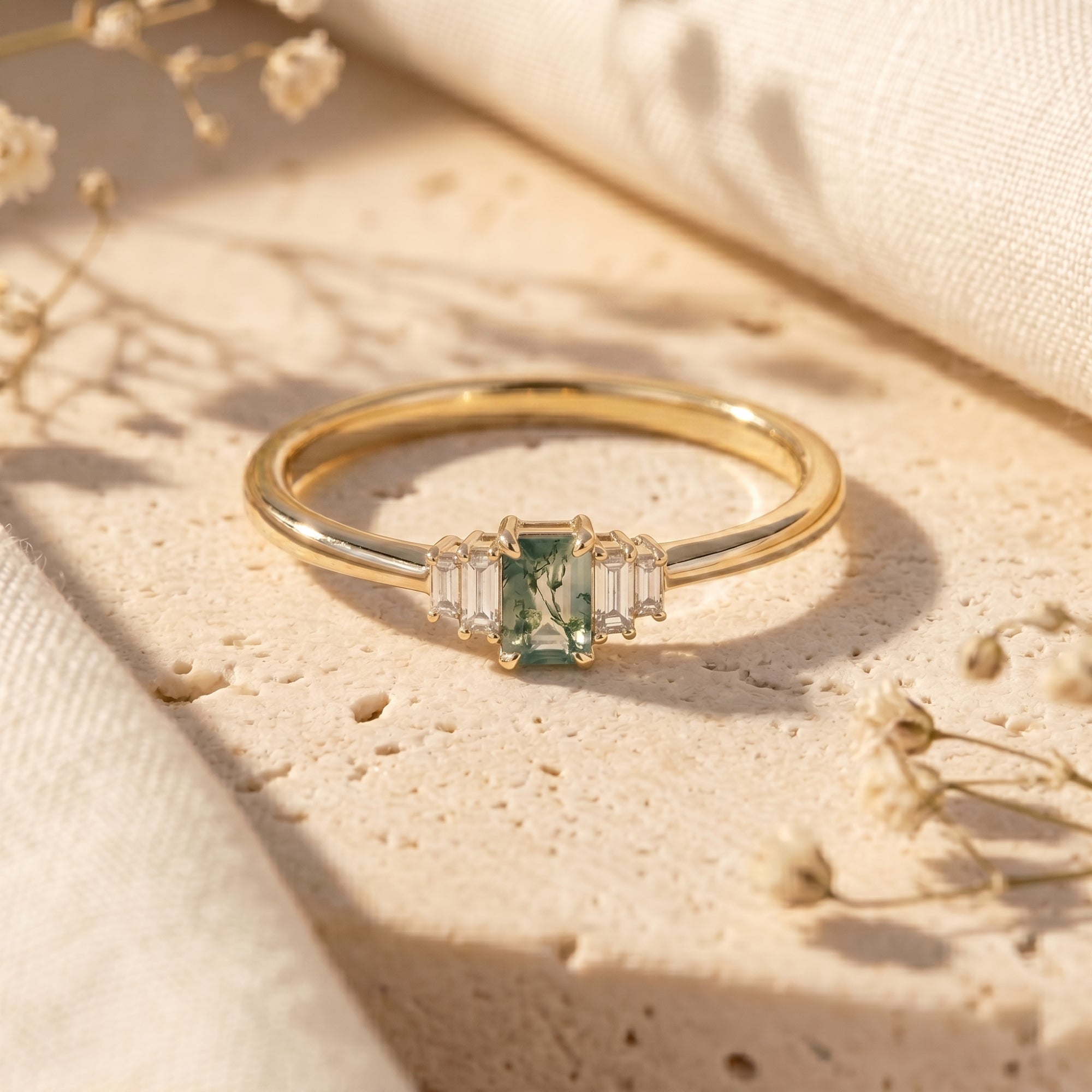 Yellow gold emerald-cut green moss agate ring with baguette accents on a textured stone background.