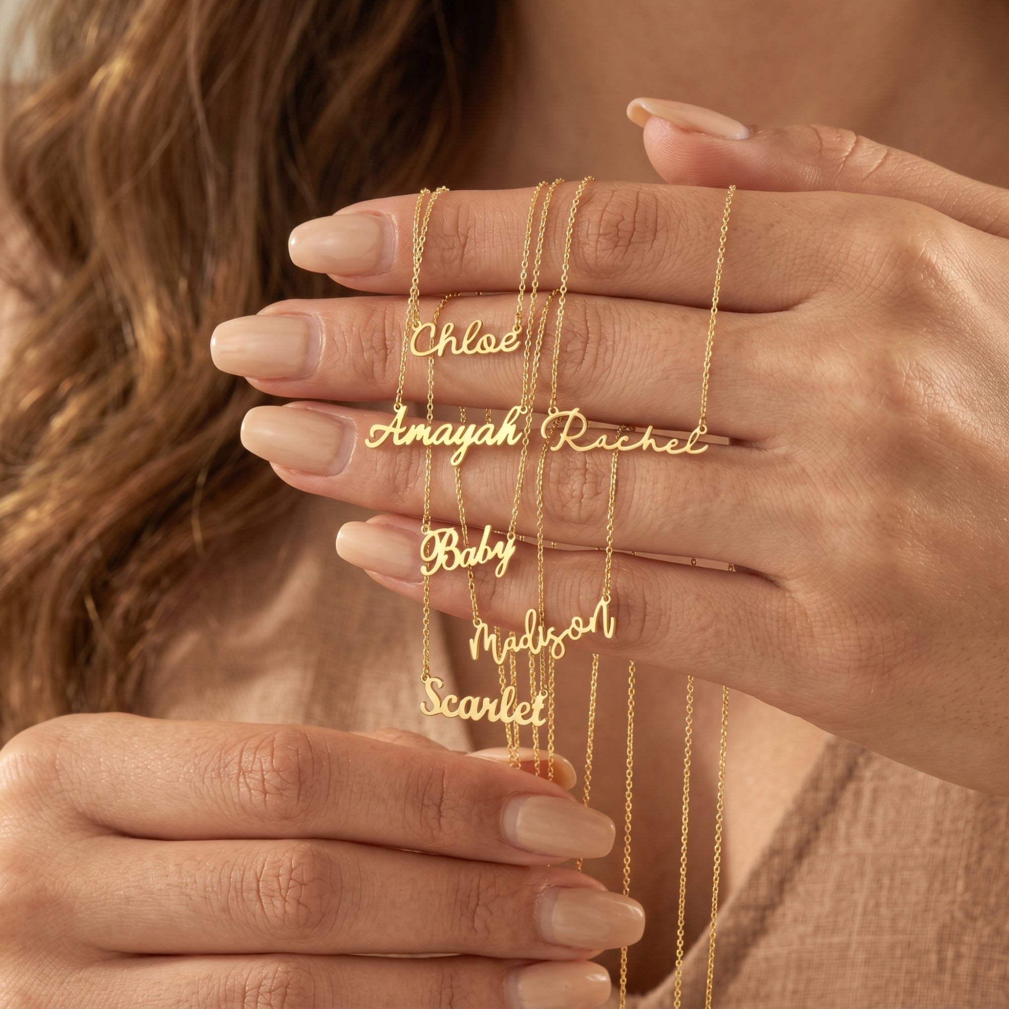 Hand holding several 18K gold finish custom name necklaces to demonstrate size and various script font styles.