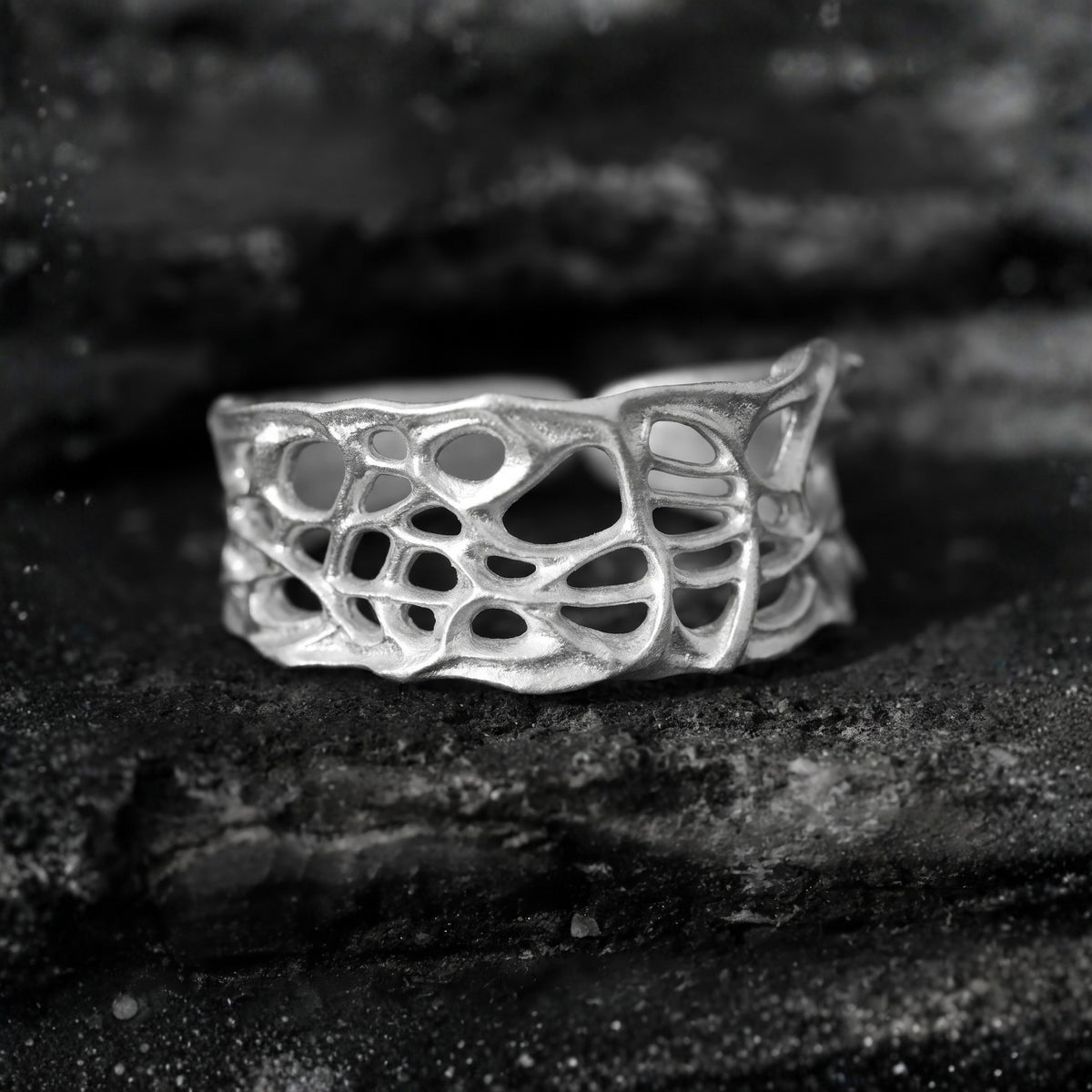 Front close-up of the fine-silver open band ring showing its sculpted organic openwork on rough dark rock.