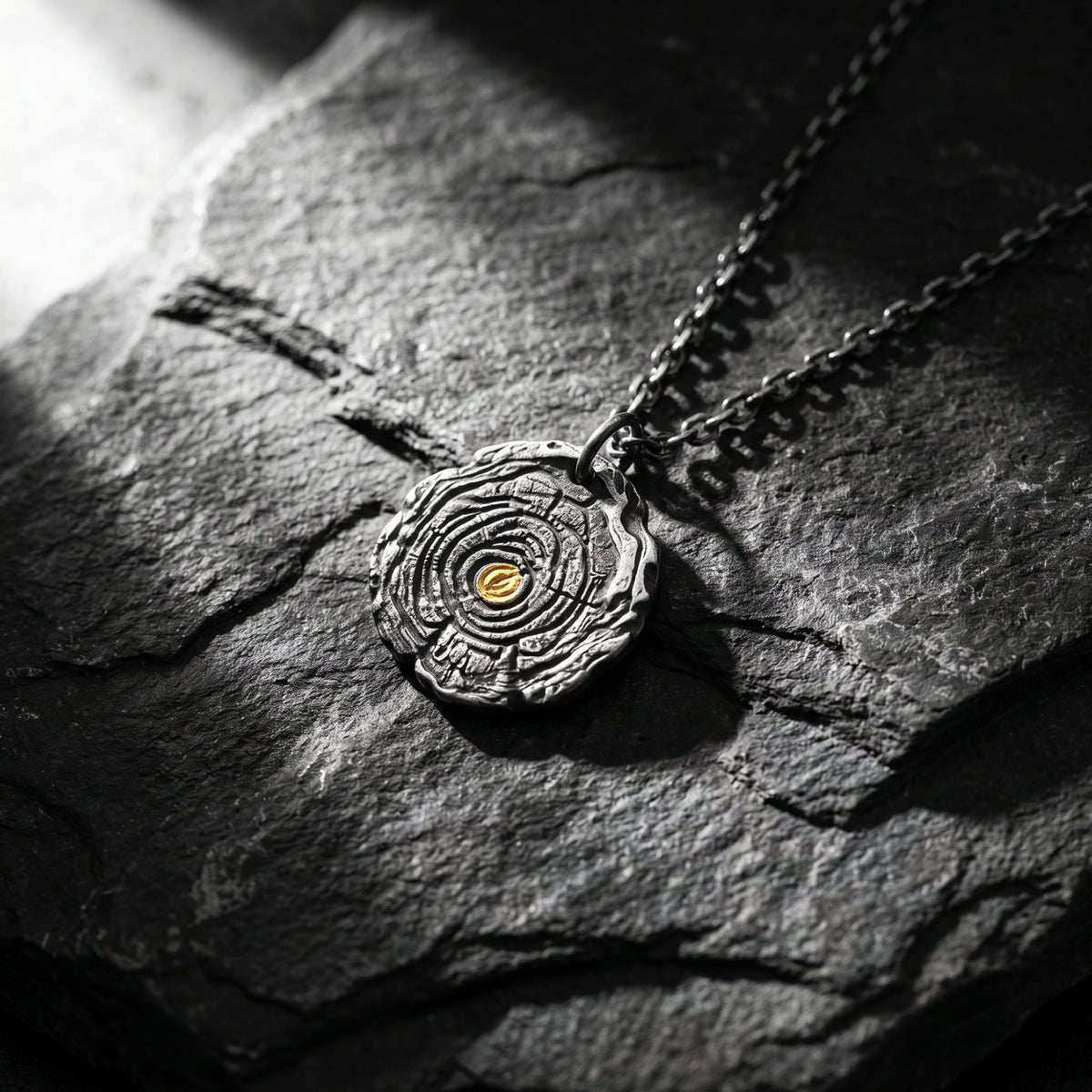 Close-up of the silver growth ring pendant lying on textured dark stone.
