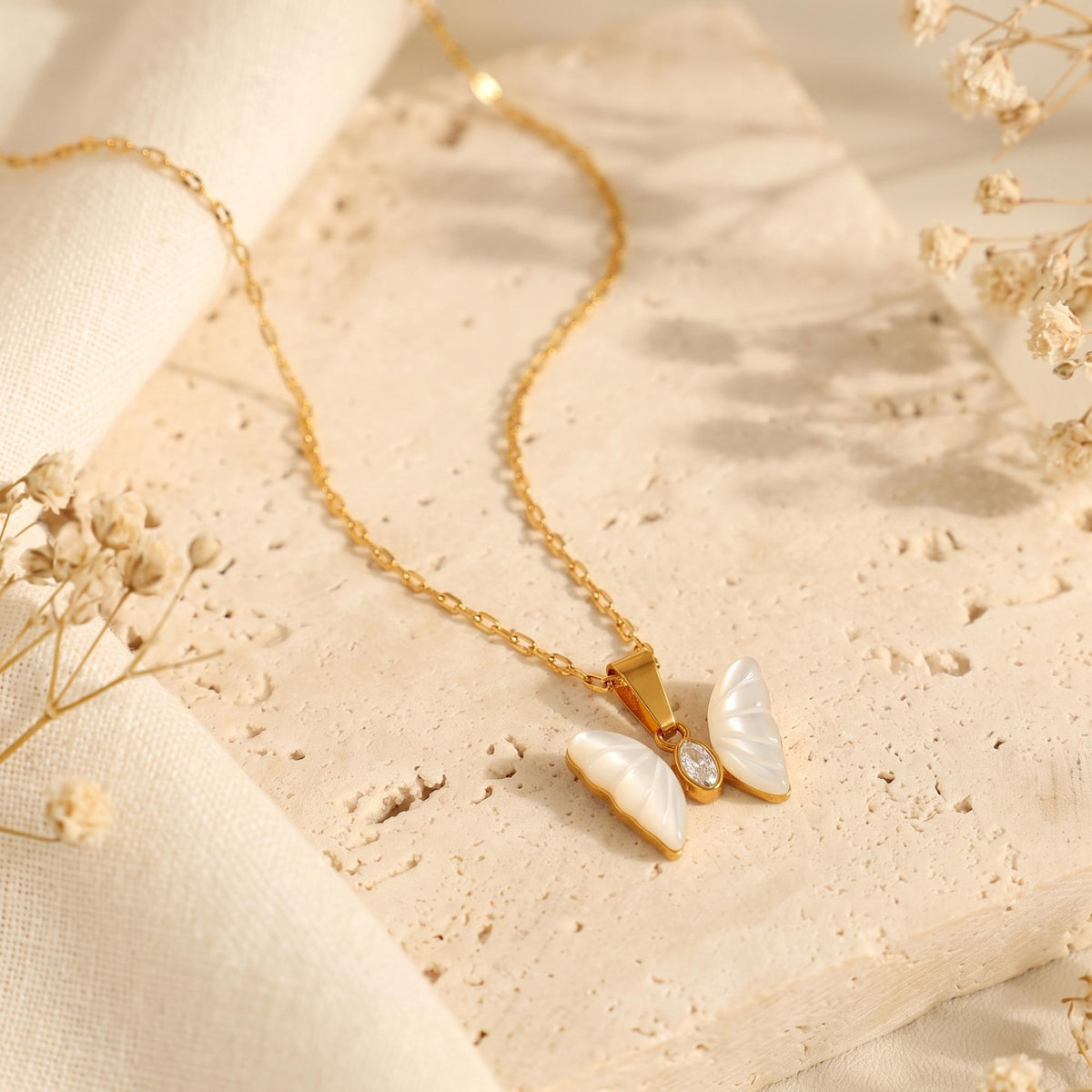 Alternate view of the mother-of-pearl butterfly pendant with a gold-tone chain on travertine stone.