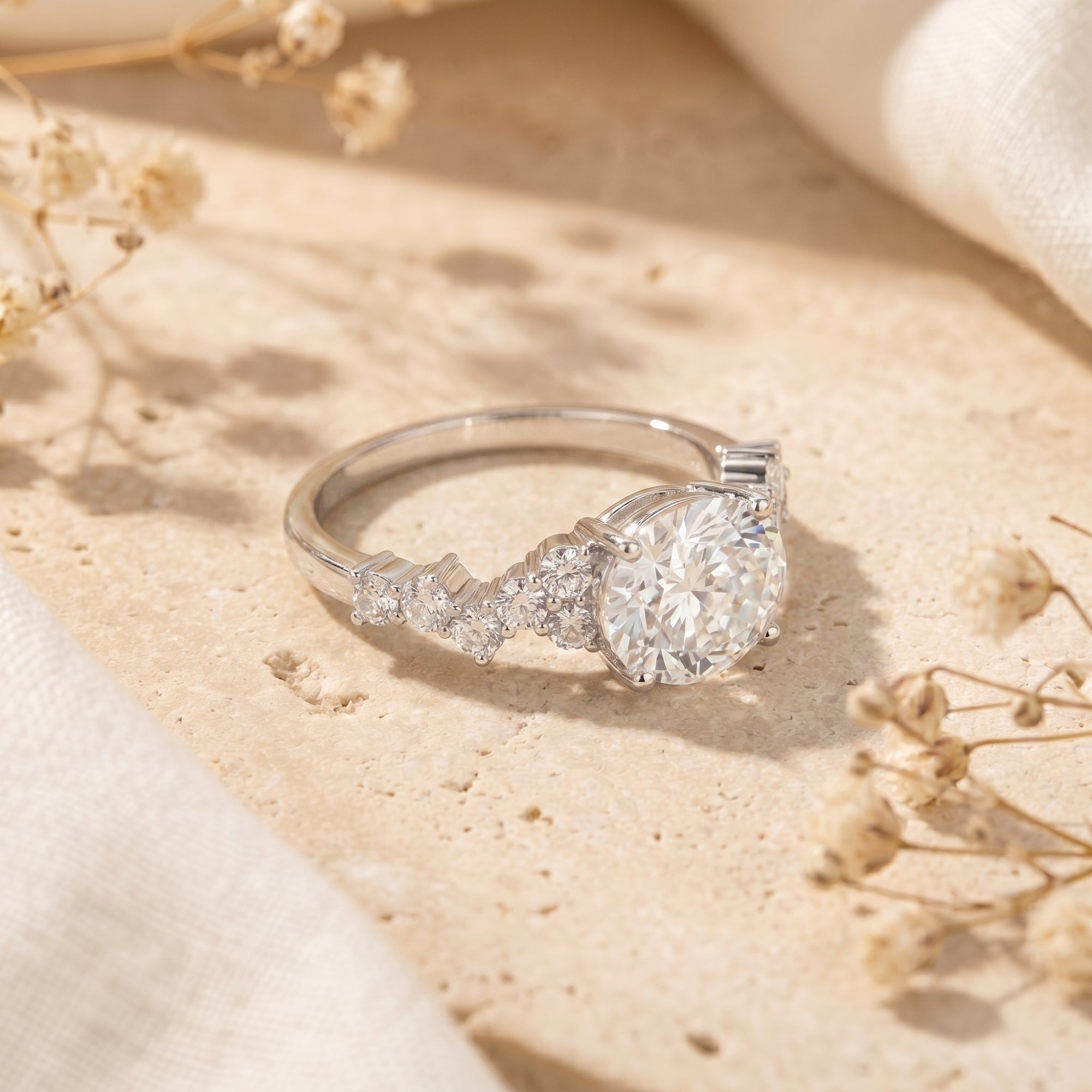 Side view of the silver oval moissanite ring showing the intricate cluster pavé setting on a stone surface.