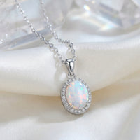 Oval opal pendant necklace in solid gold, with a white opal, displayed on white silk fabric.