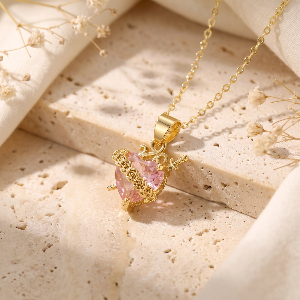 Angled close-up of the gold-tone pink heart pendant with rose vines and dagger motif.