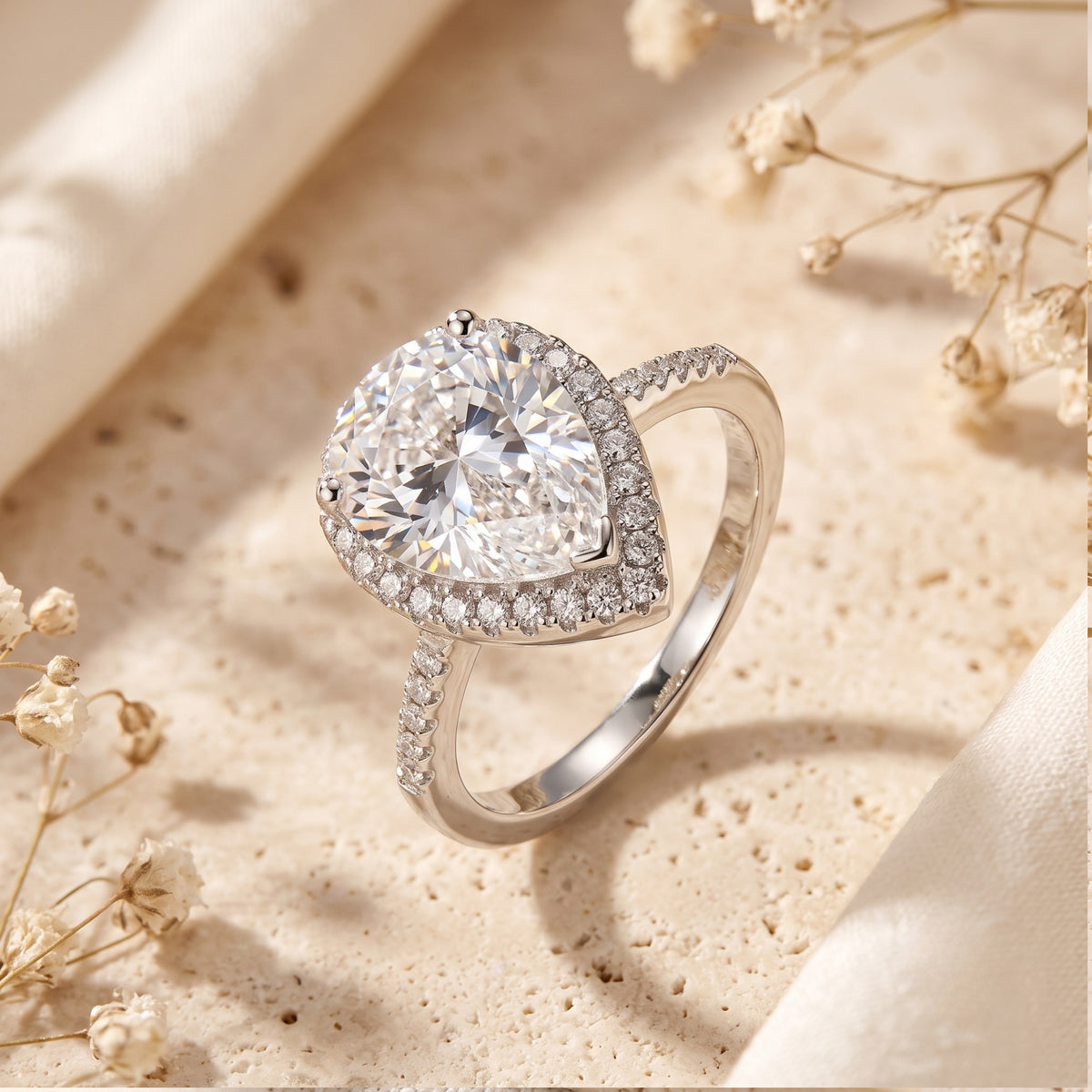 Angled close-up of a silver ring highlighting its raised pear-cut center stone, halo, and pavé band.