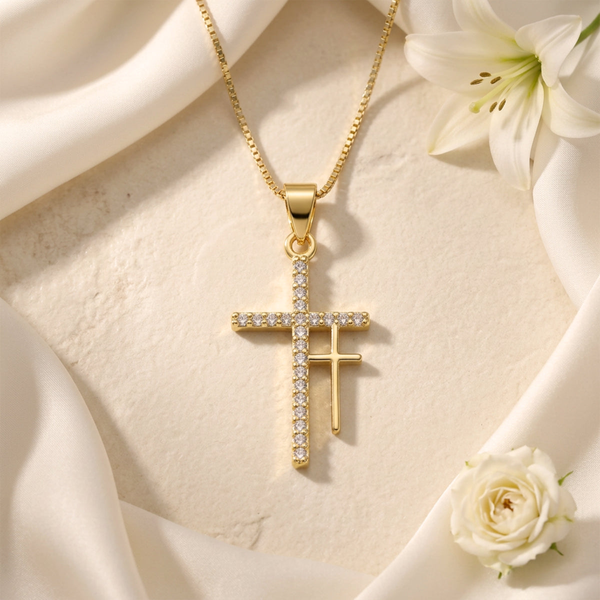 Centered top-down view of the gold-tone double cross pendant on beige stone surrounded by white fabric