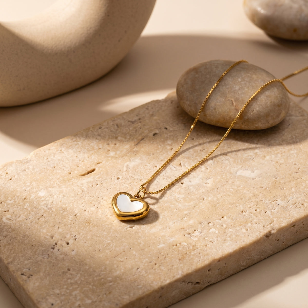 Detail view of the gold Leonore heart necklace with white inlay on a natural stone surface.