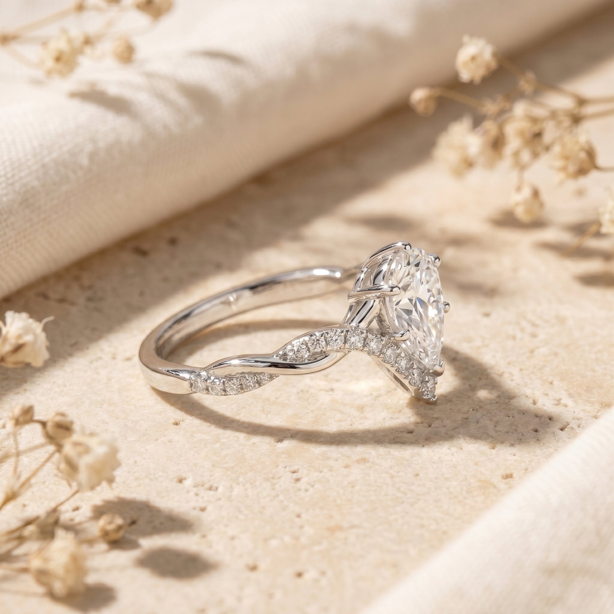 Side profile of a silver pear-cut moissanite ring showing the intricate twisted band and elevated stone setting.