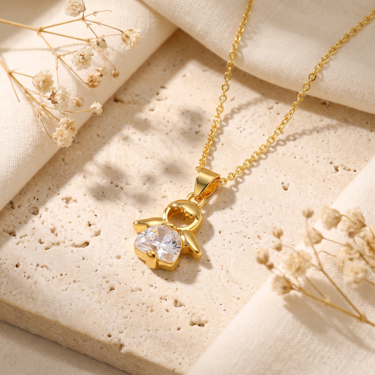 Angled close-up of the gold-tone angel pendant with clear crystal gown resting on textured stone.