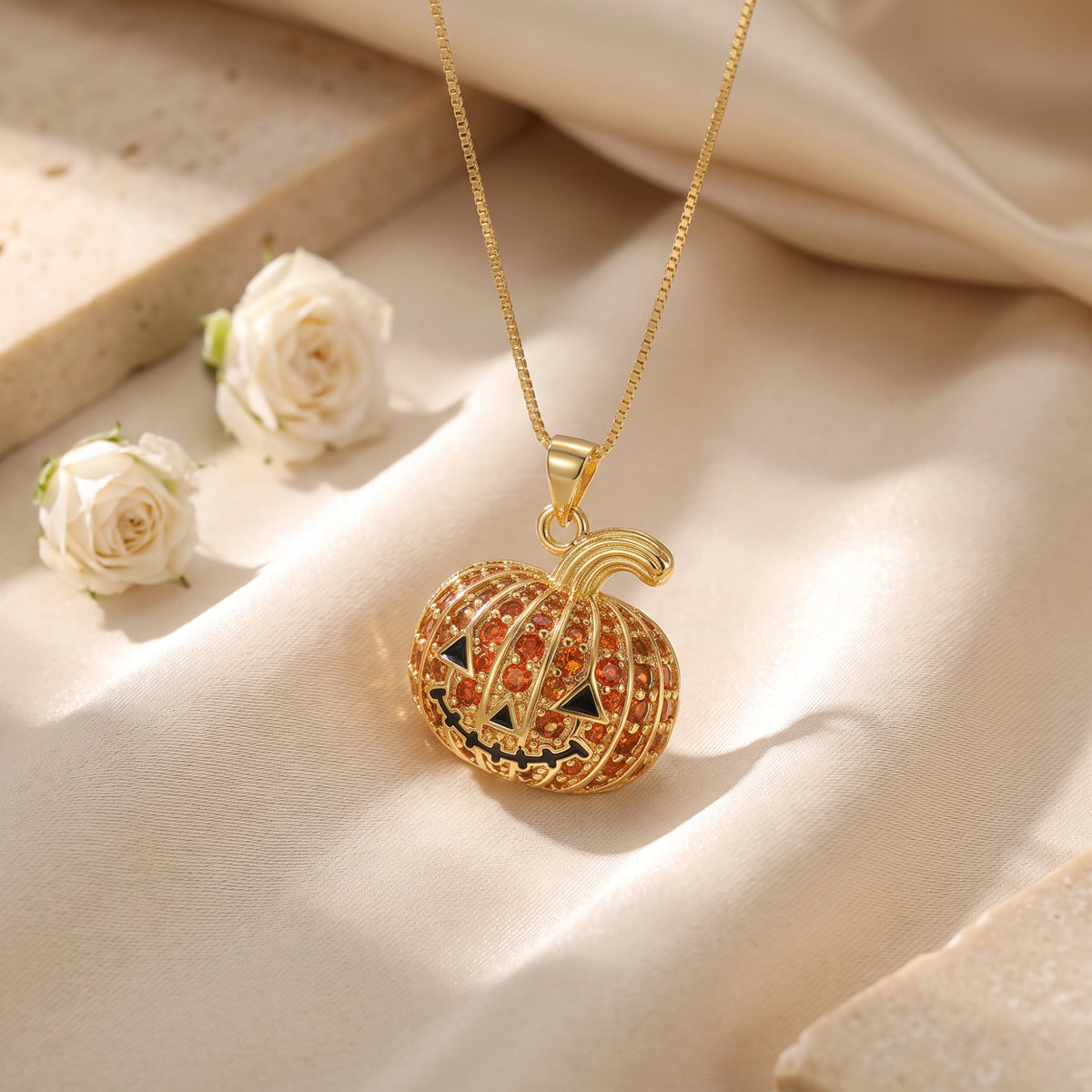 Gold-tone pumpkin pendant necklace resting on draped light-colored fabric with white flowers in the background.