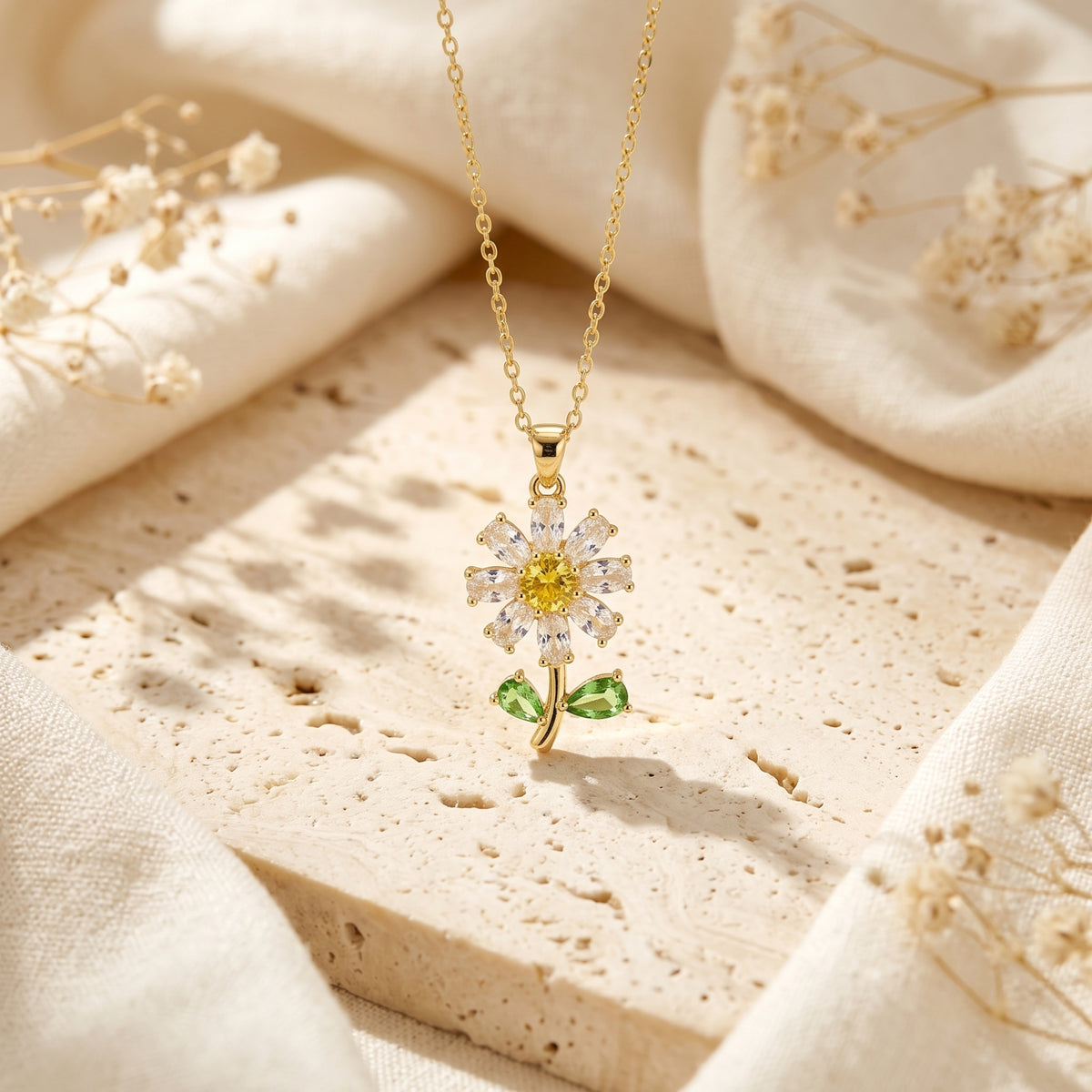 Gold-tone daisy pendant necklace hanging vertically over a textured beige stone block.