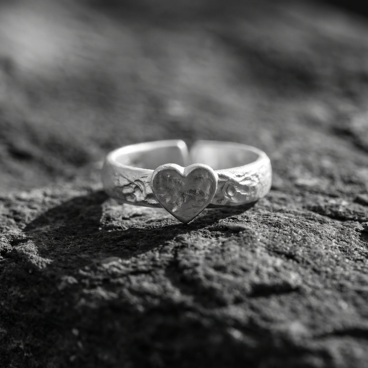 Frontal view of the hammered heart ring with its textured heart face resting on rock.