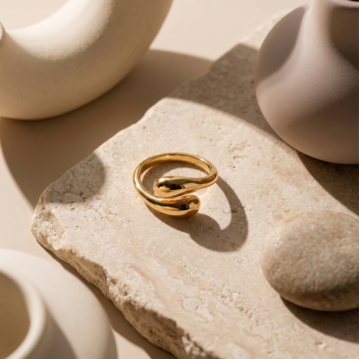 Polished 18K gold vermeil bypass ring displayed on a stone slab among minimalist ceramic decor.