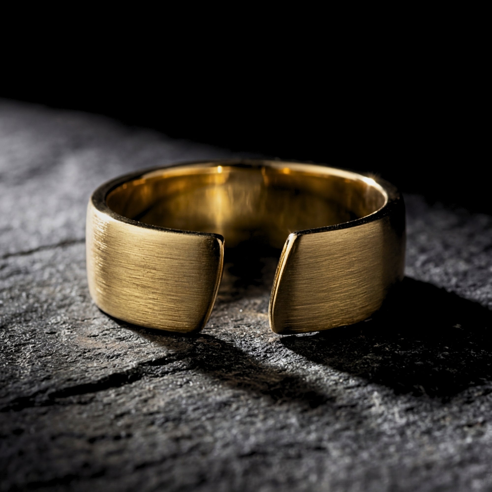 Macro view of the open band on a gold stainless steel gap ring resting on a textured stone surface.