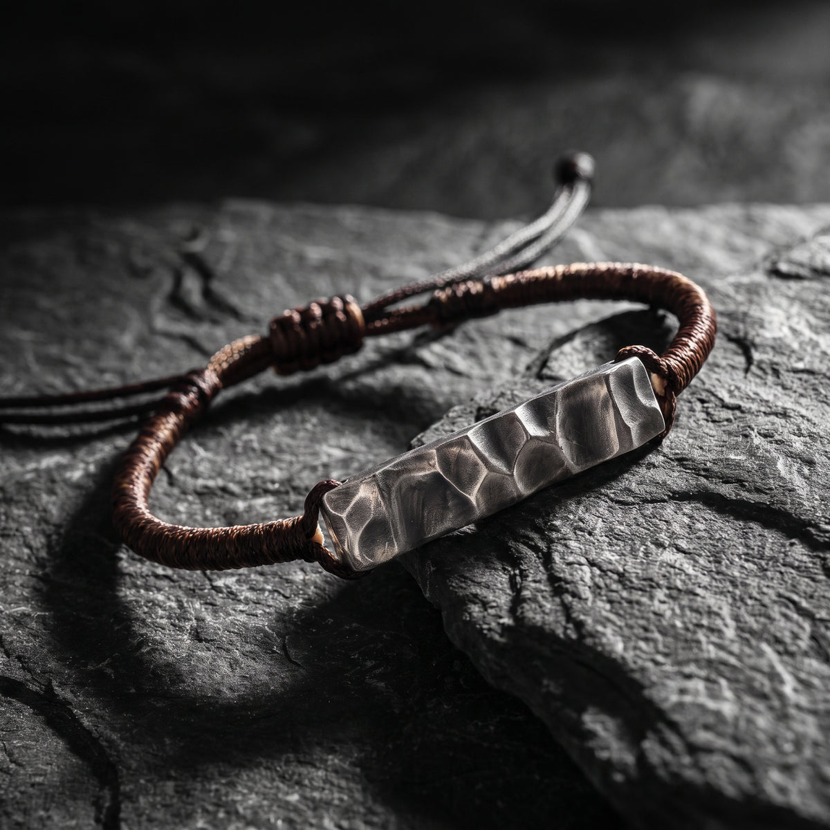 Angled close-up of the textured silver hammered bar bracelet displayed on dark rock.
