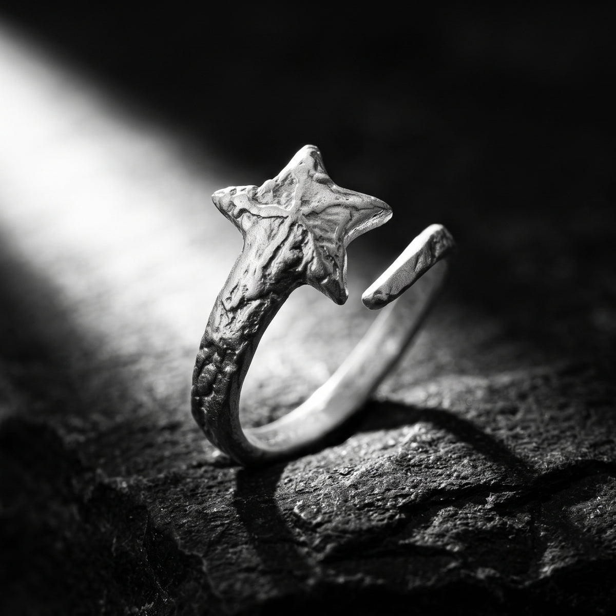 Upright silver star open ring highlighted by a beam of light on a textured dark surface.