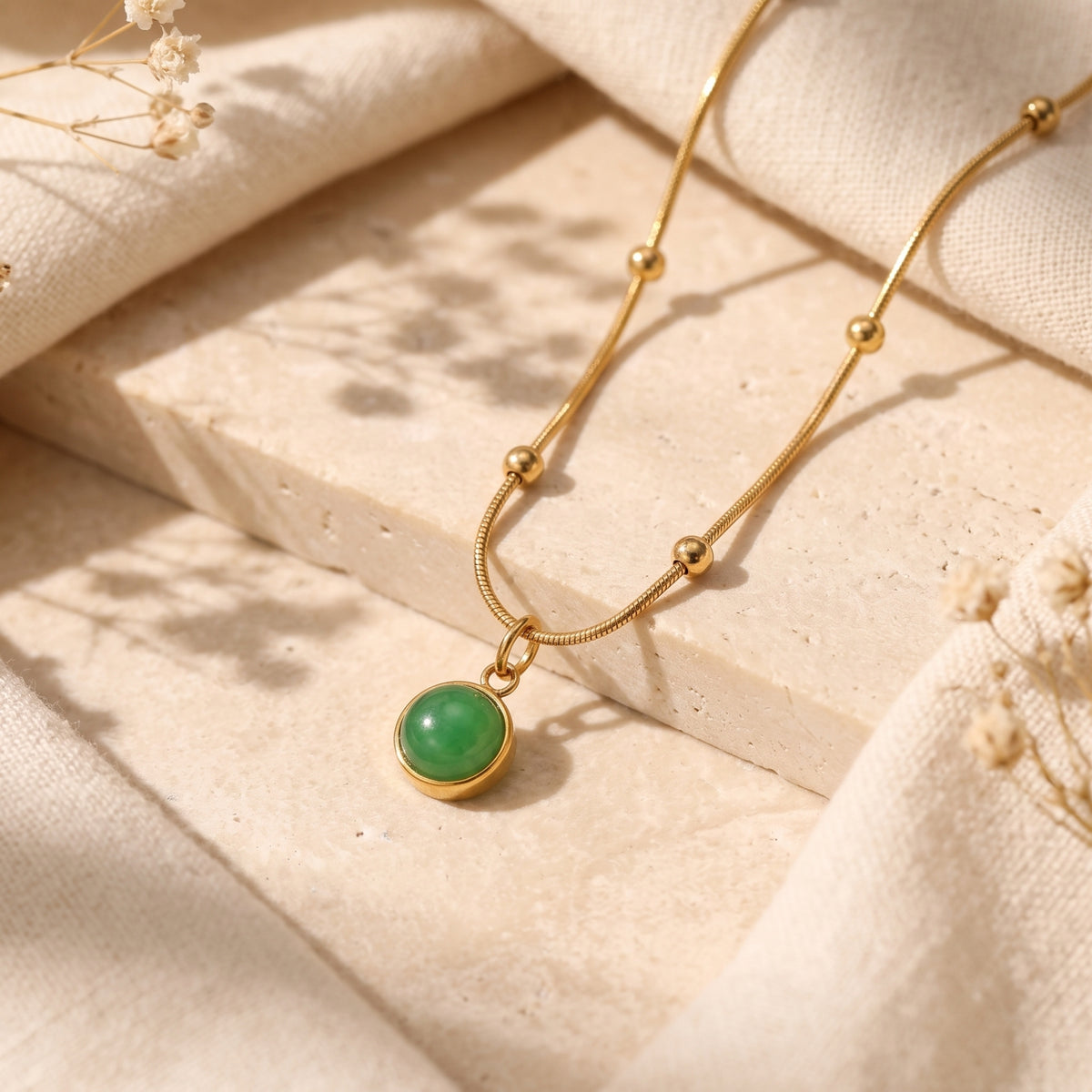 Gold-tone station-bead necklace with a round green agate pendant displayed on a pale textured slab.