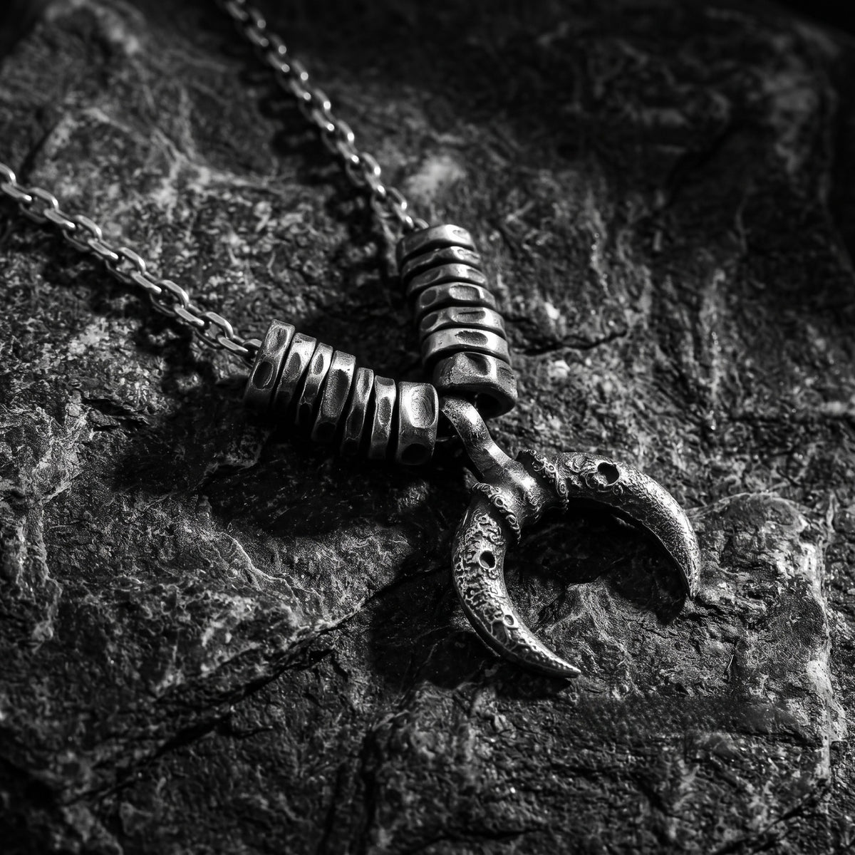 Close-up of the crescent pendant and textured spacers resting on dark textured stone.