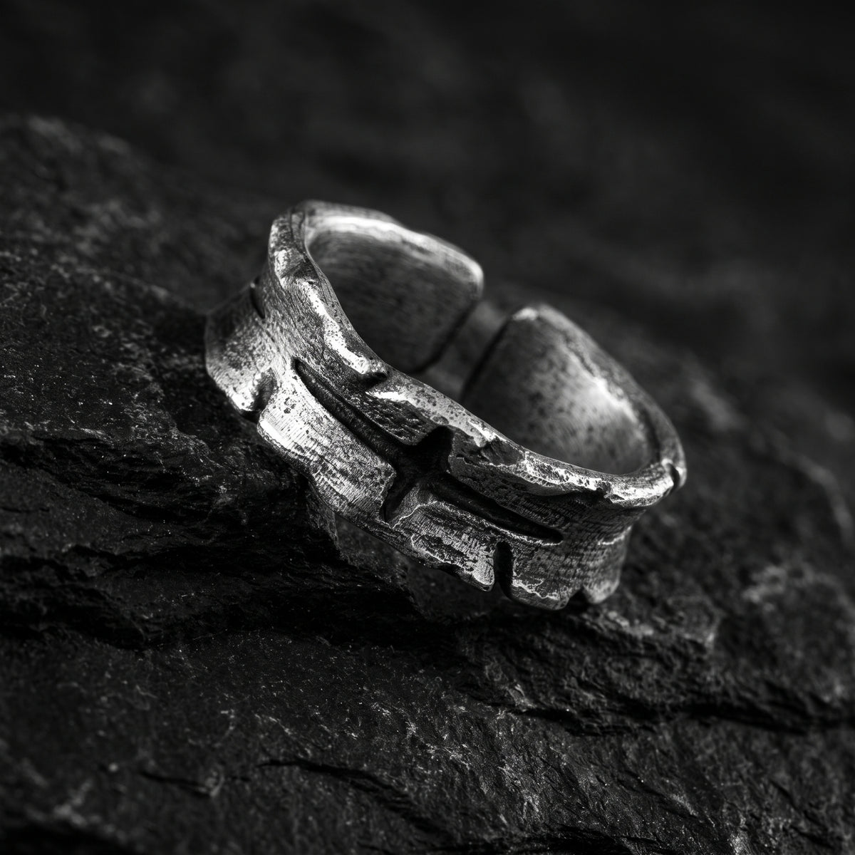 Angled view of the silver cross open band ring on a dark textured stone surface, showing its open gap.