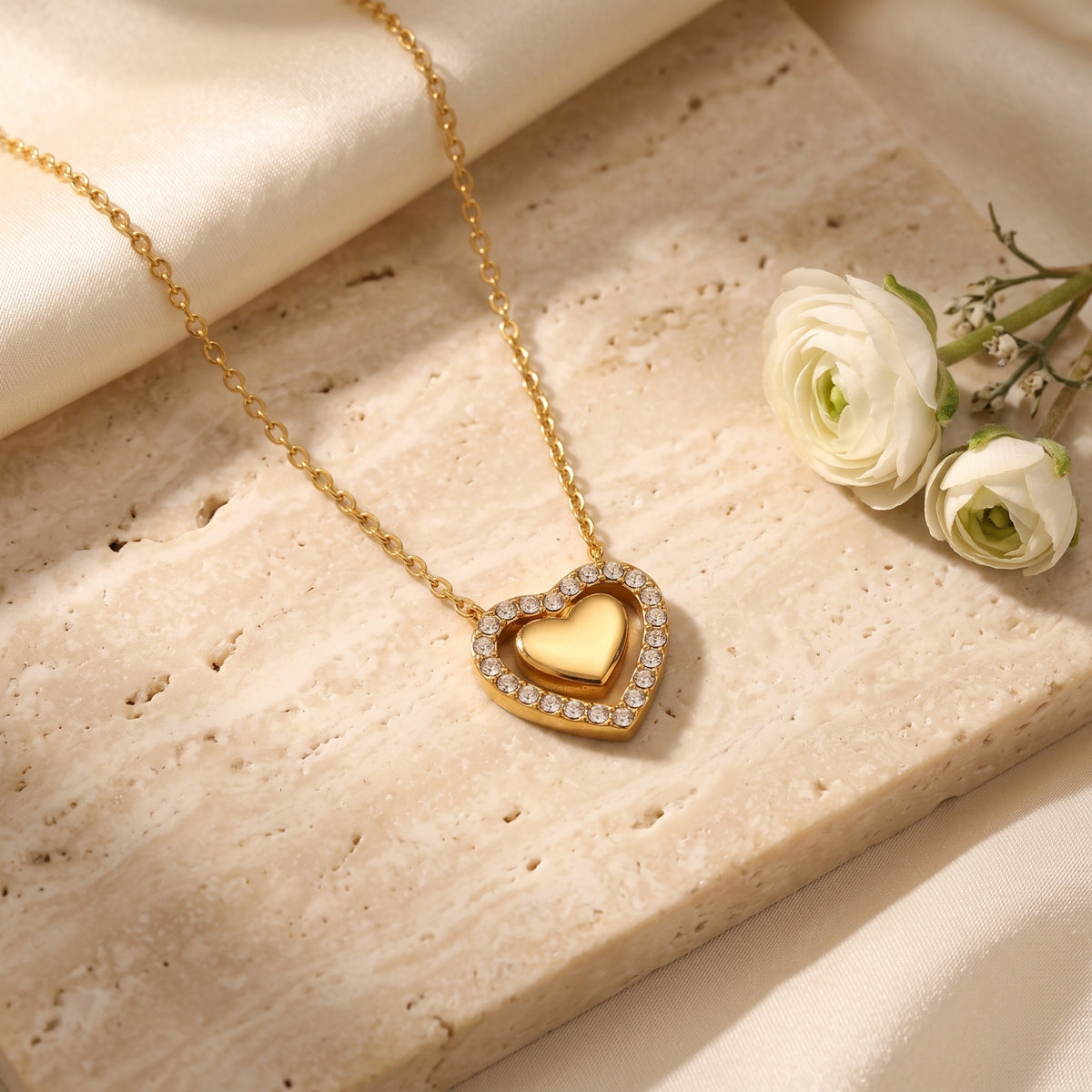 Close-up of an 18K gold PVD finished double heart necklace with round cut simulated diamonds on a stone surface.