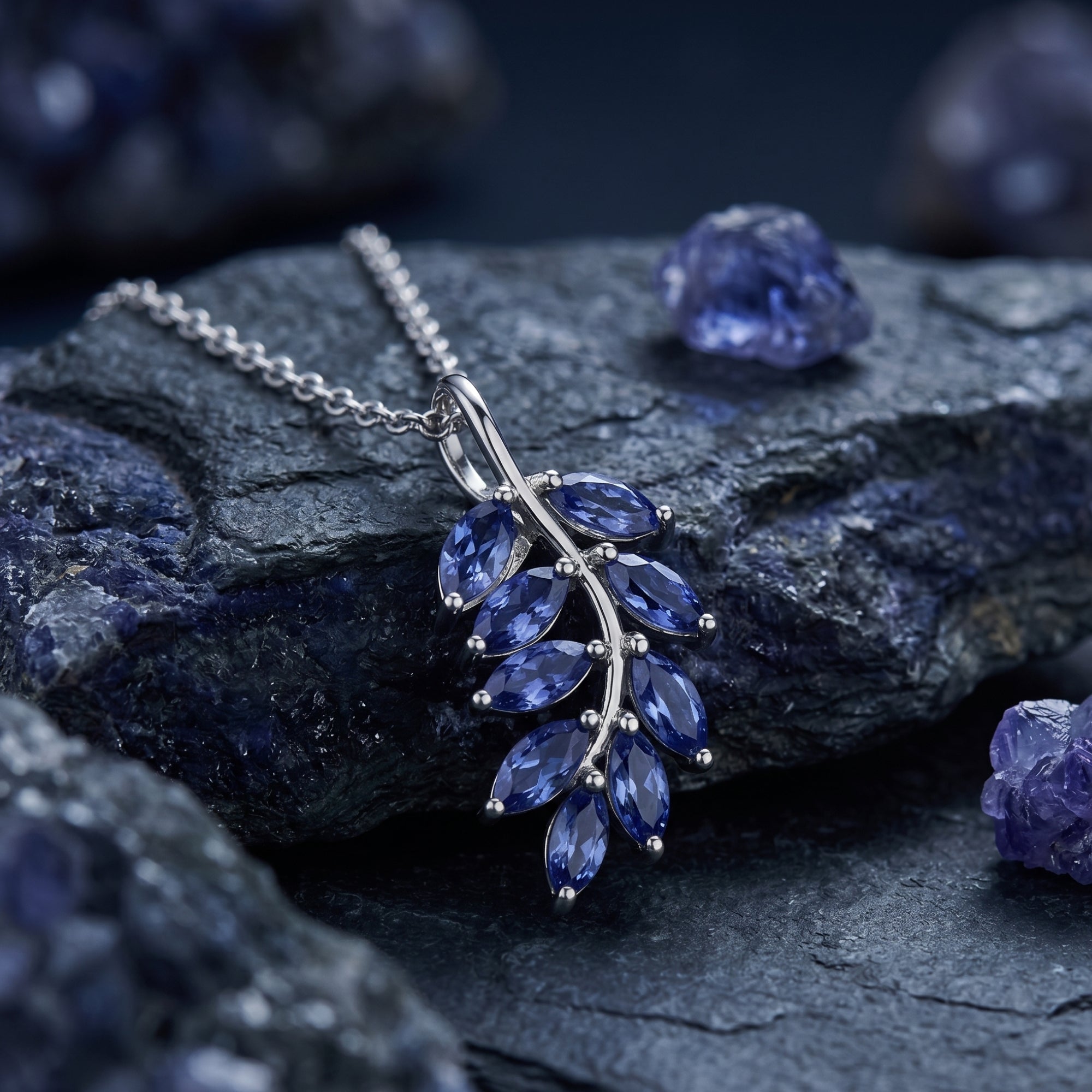 Marquise tanzanite leaf pendant in sterling silver shown on a dark textured rock with raw tanzanite gems.