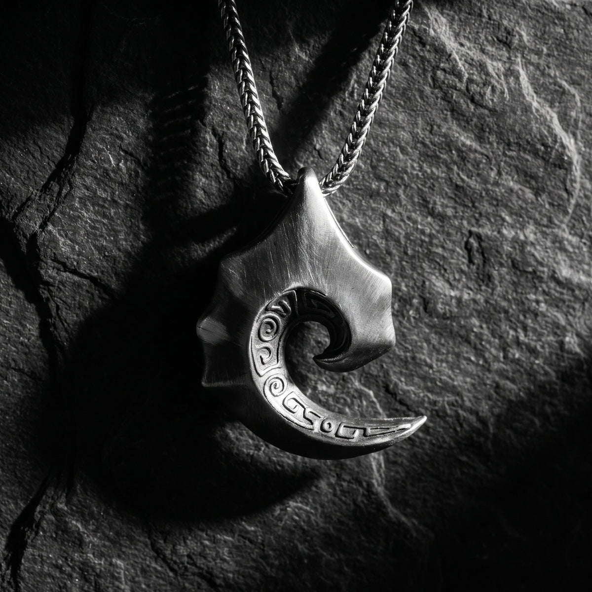 Front view of the silver tidal scroll pendant hanging on a chain against a dark stone backdrop.