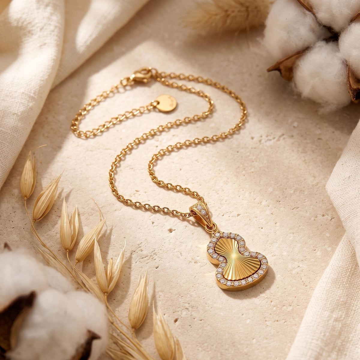 Gold gourd pendant necklace with cubic zirconia halo on textured surface with dried botanicals.