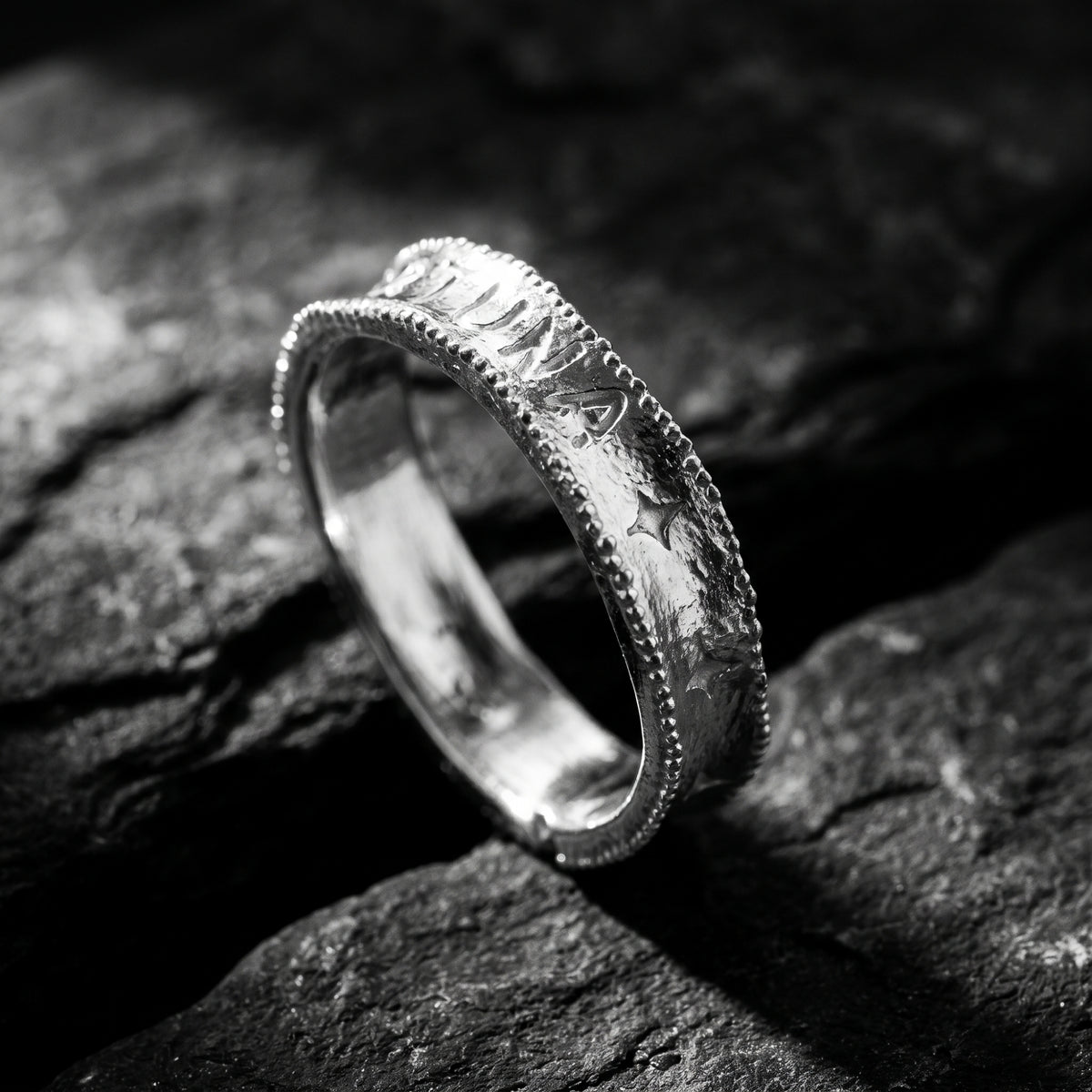 Angled macro view of the silver ring on dark stone, showcasing engraved star accents and milgrain edges.
