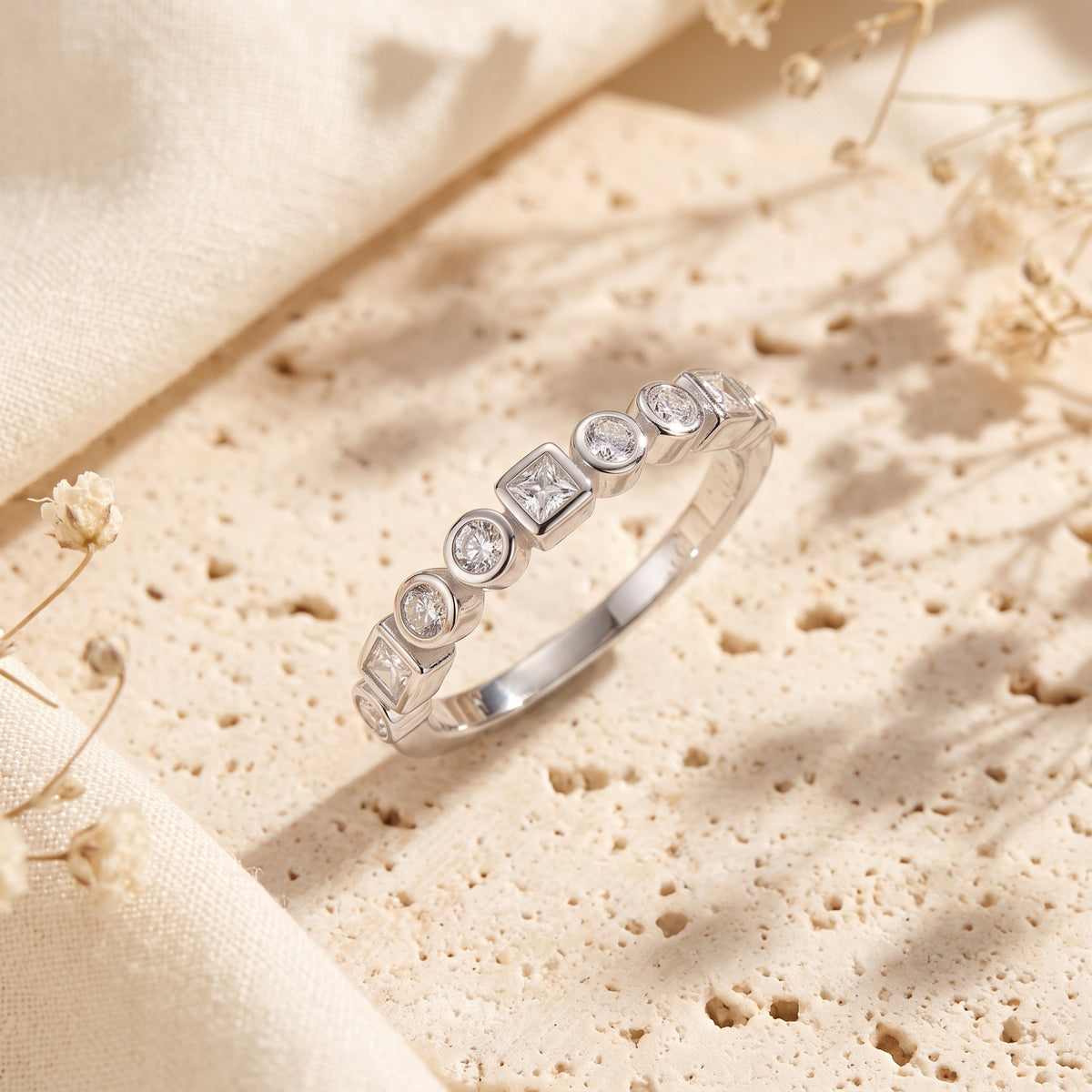 Close-up of silver eternity band showing alternating round and princess-cut stones in bezel settings.