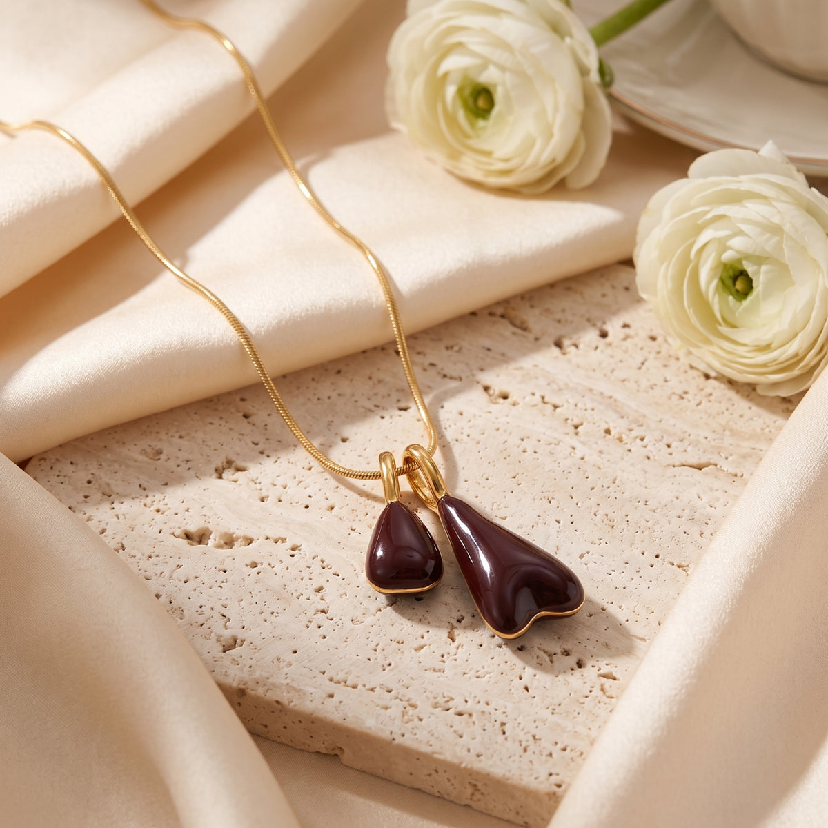 Detail of the Marais gold pendant necklace showing the high-gloss burgundy double drops on a textured stone.