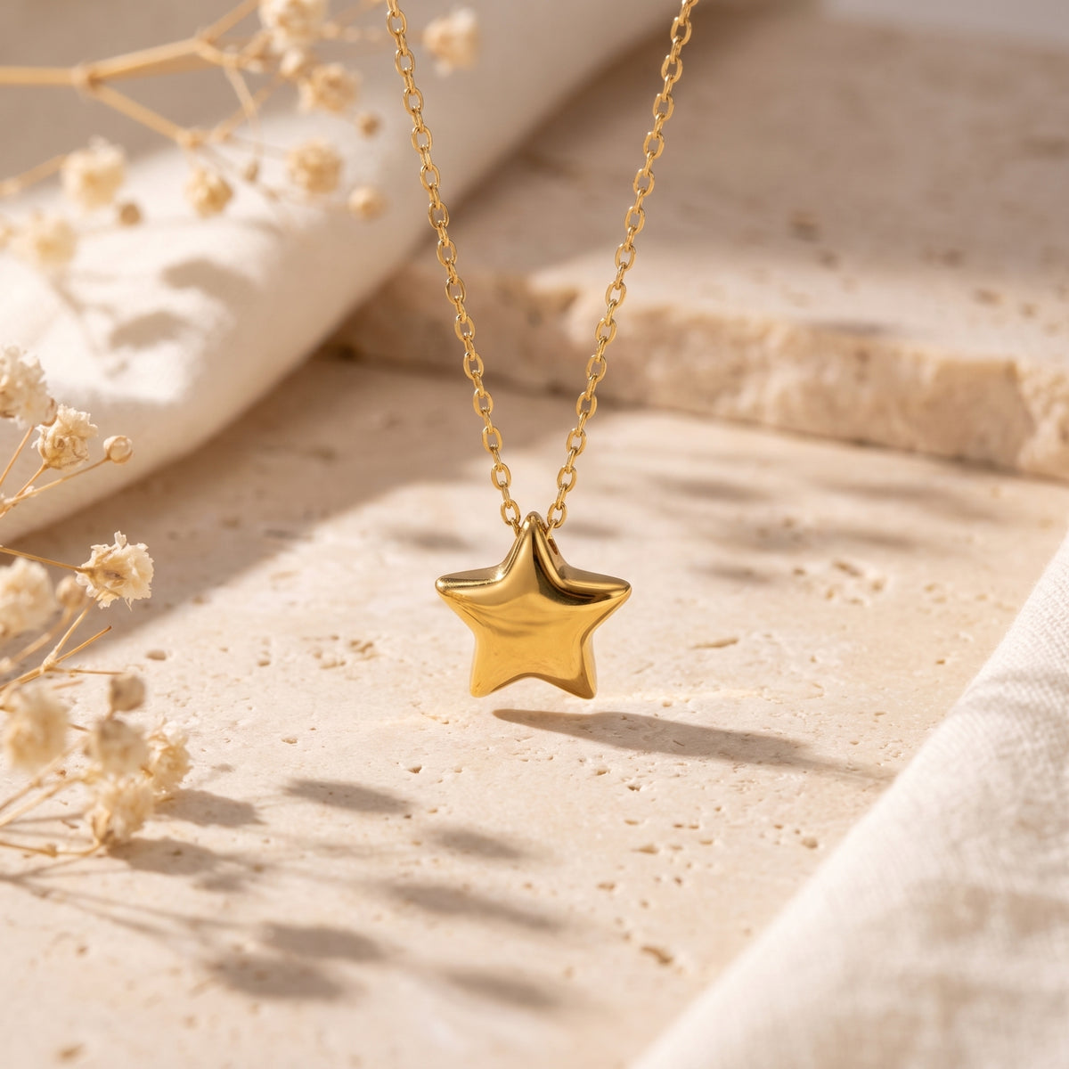 Close-up of the gold-tone puffed star pendant suspended above a beige stone surface.