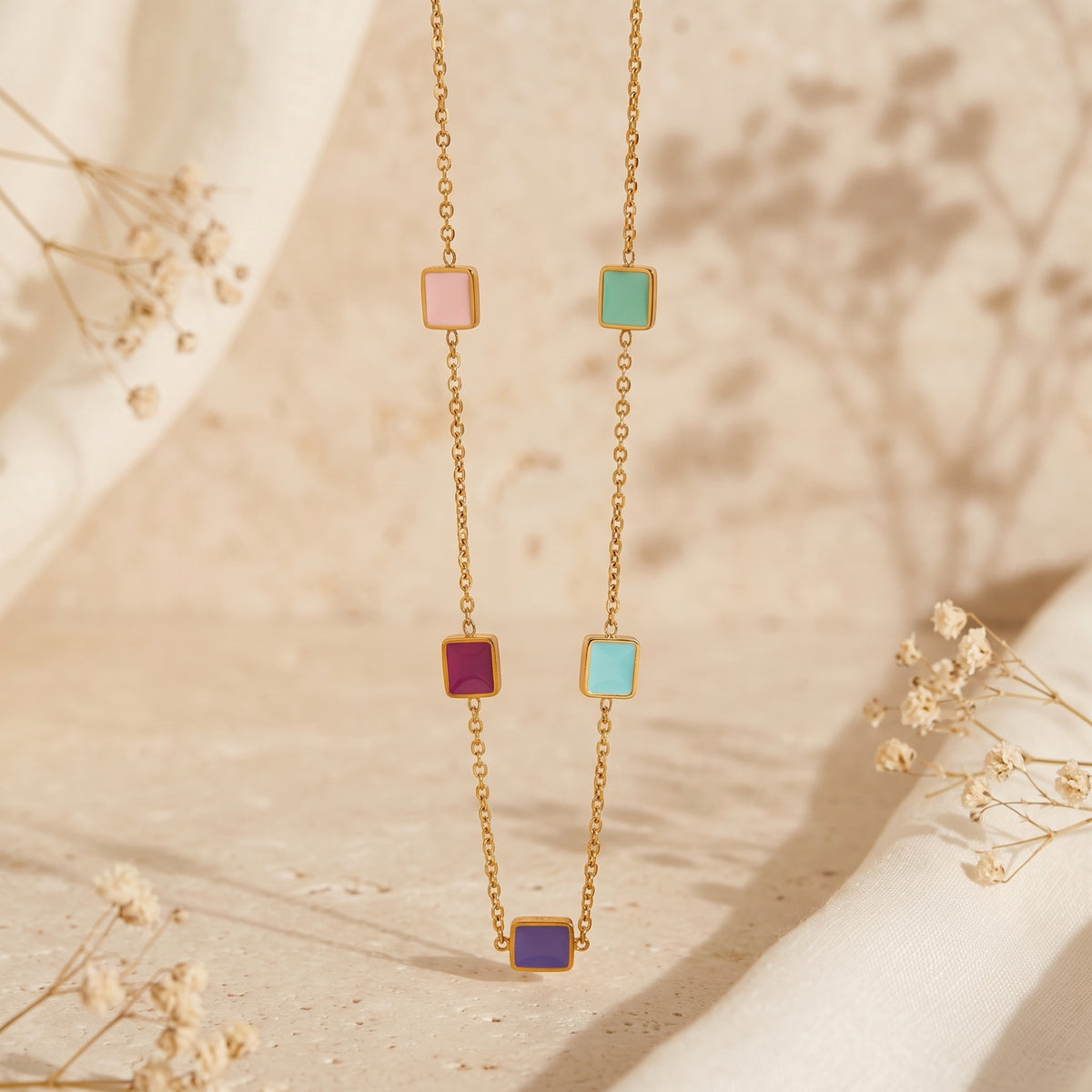 Front view of a gold-tone necklace hanging vertically with five colorful enamel square stations.